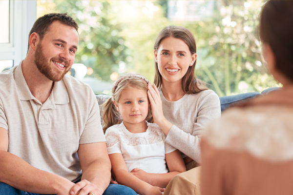 Mann, Frau und Kind mit Blick zu einer Frau, die mit dem Rücken zur Kamera sitzt