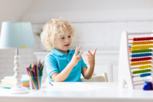 Junge rechnet mit den Händen und sitzt am Schreibtisch