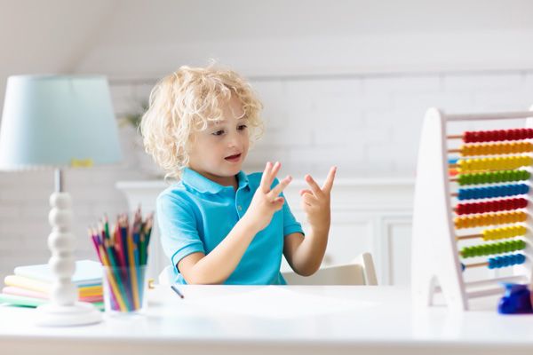 Junge rechnet mit den Händen und sitzt am Schreibtisch