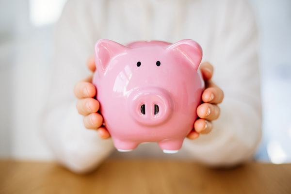 Person im Hintergrund hält eine rosa Sparschwein, das im Vordergrund zu sehen ist