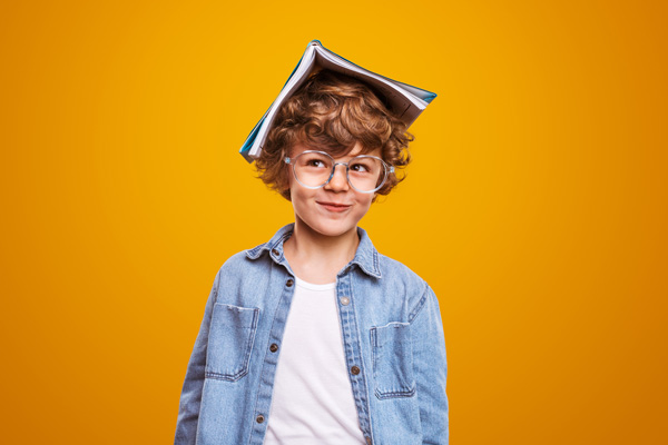 Junge mit Brille und Heft auf dem Kopf vor orange farbenen Hintergrund