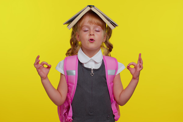 Mädchen mit Rücksack, geschlossenen Augen und einem Buch auf dem Kopf auf gelbem Hintergrund