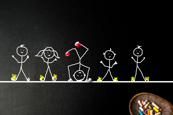 Schwarze Tafel mit weißen Strichmännchen darauf gemalt, ein Kreidebehälter im Vordergrund